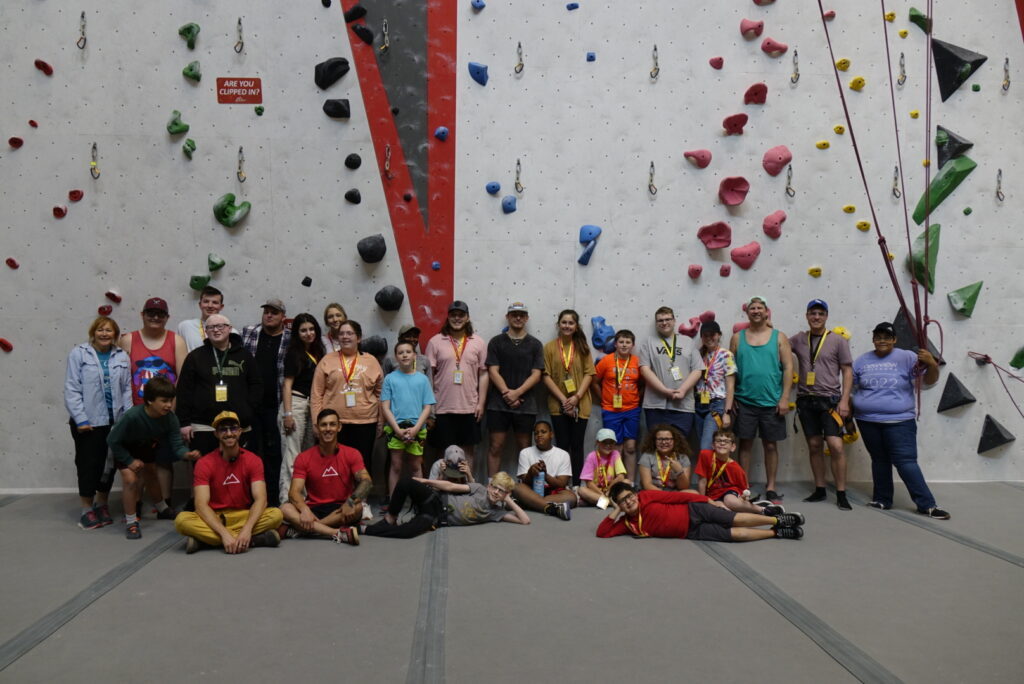 Campers posing for a group photo in front of the rock climbing wall at Threshold Climbing gym.