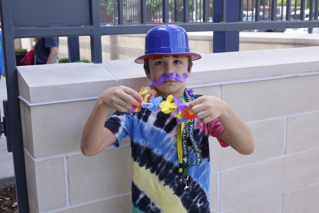 A camper dressed up in a goofy hat a fake mustache having a blast at the camp carnival.