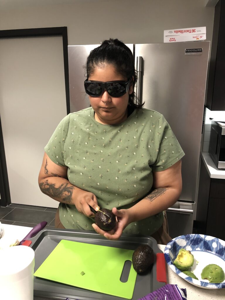 A camper wearing dark sunglasses is cutting an avocado during a cooking lesson.
