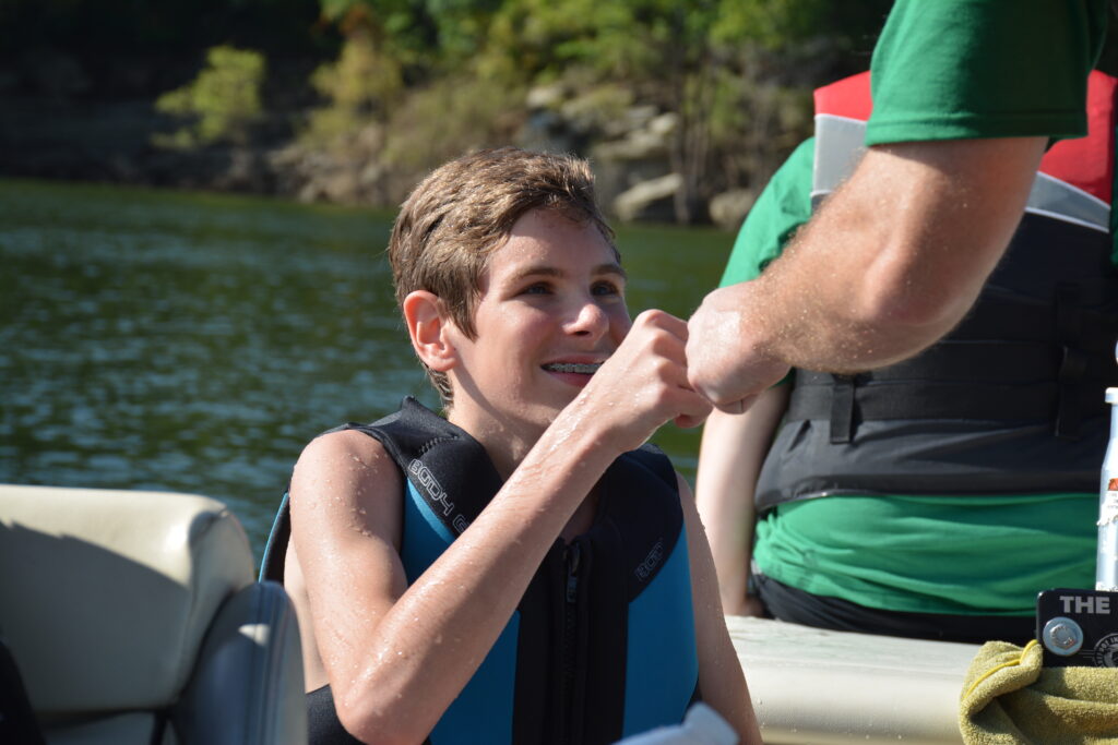 A camp counselor is offering a camper knuckles to celebrate a successful water ski attempt.