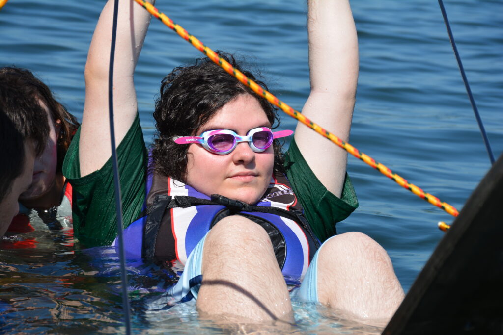 A young camper is wearing a pair of goggles and waiting for the boat captain to lift her onto skis.