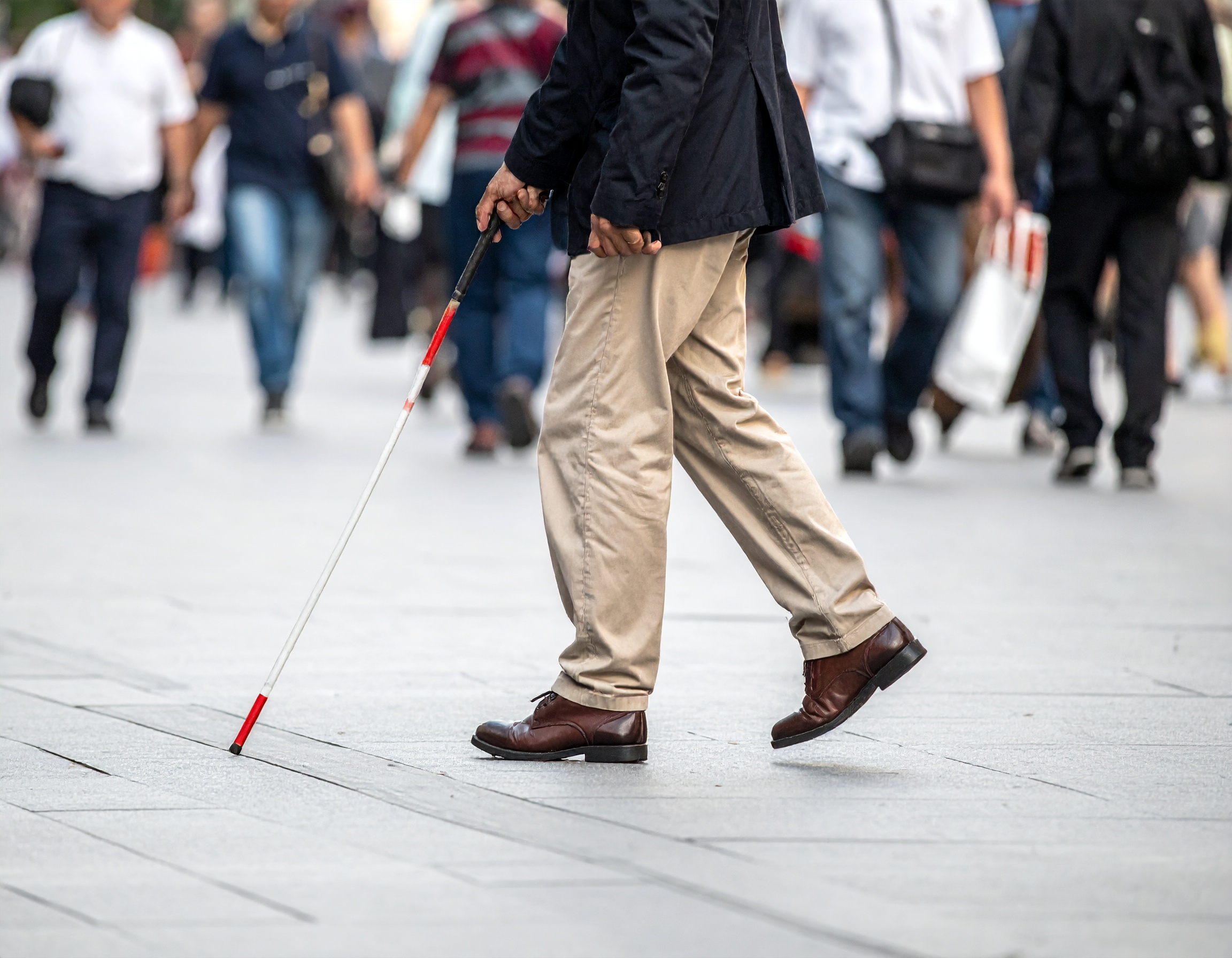 Person who is blind walking in a crowd with his white cane.