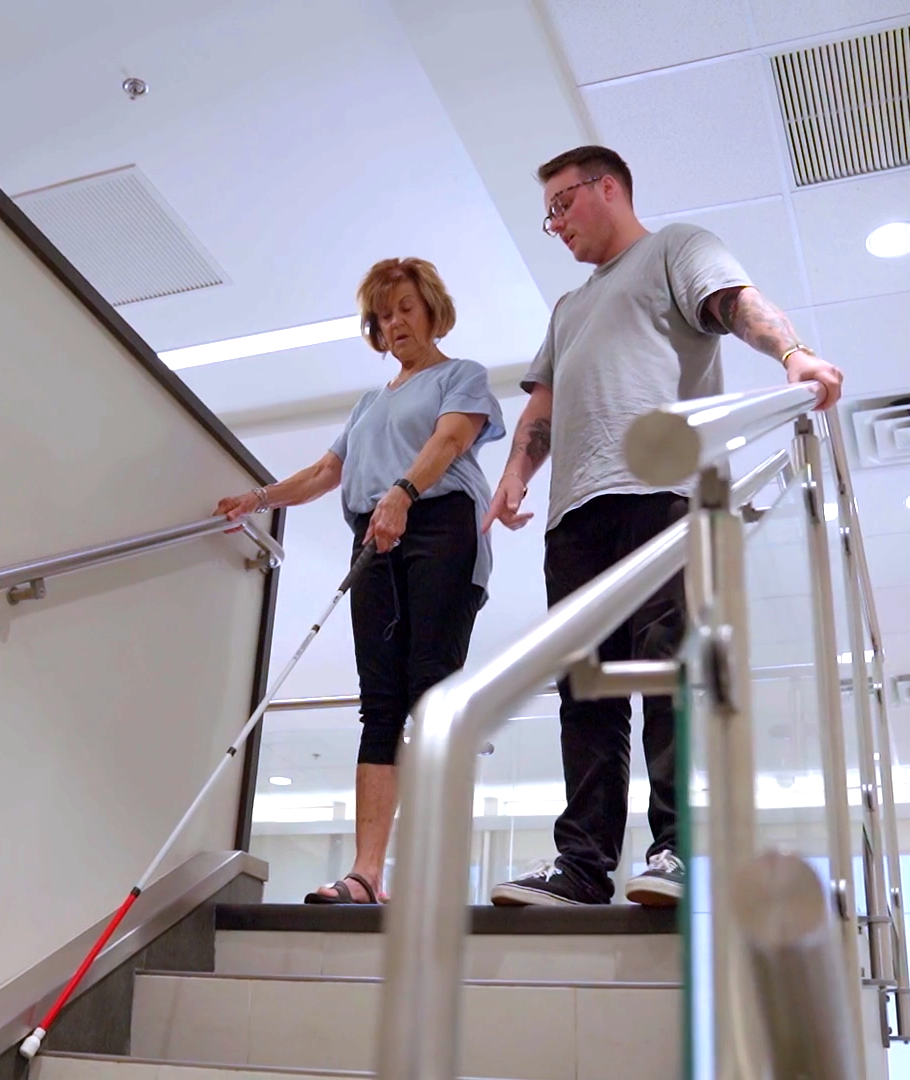 woman with cane being guided down the stairs
