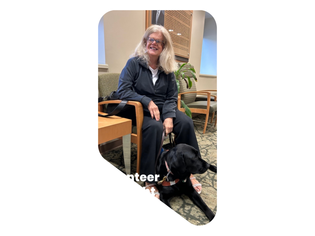 Patti sitting in a chair and smiling with her service dog at her feet.