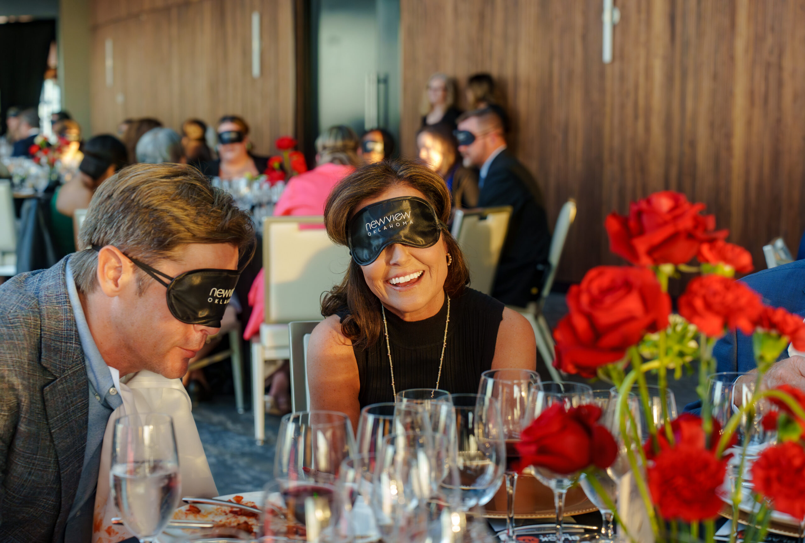 Woman wearing a blindfold smiling at the table with red roses next to her at the OKC 2026 Blackout Banquet.