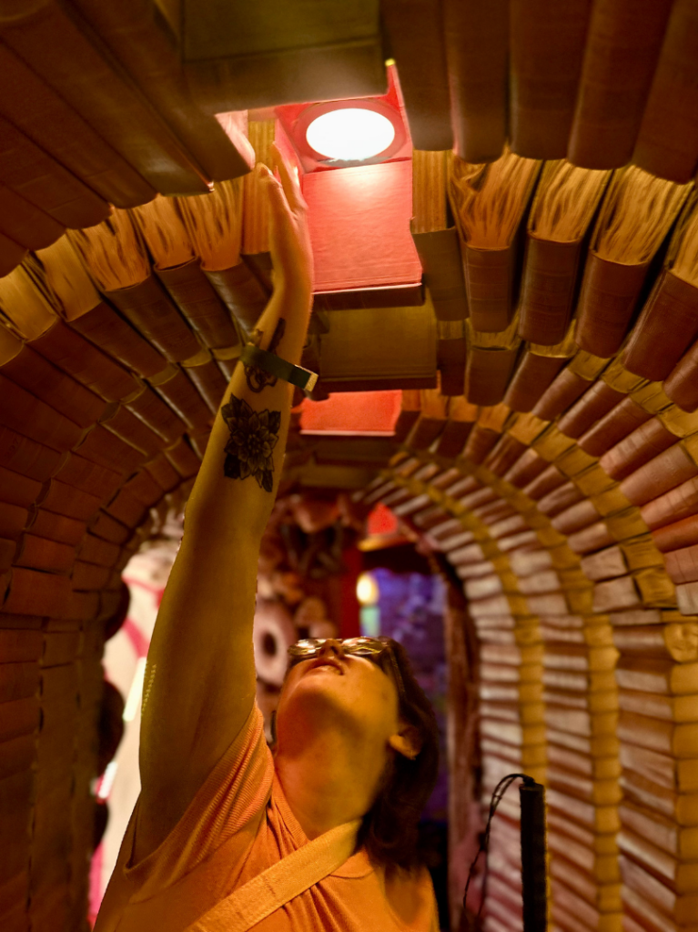 Alex standing in a hallway made entirely out of books reaching for a light.