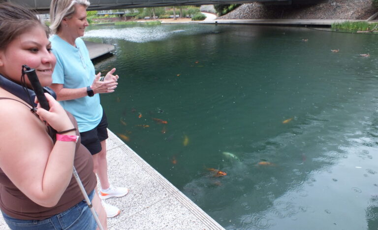 Serenity smiling at Myriad Gardens next to koi fish in pond and NewView's Christi Dixon.