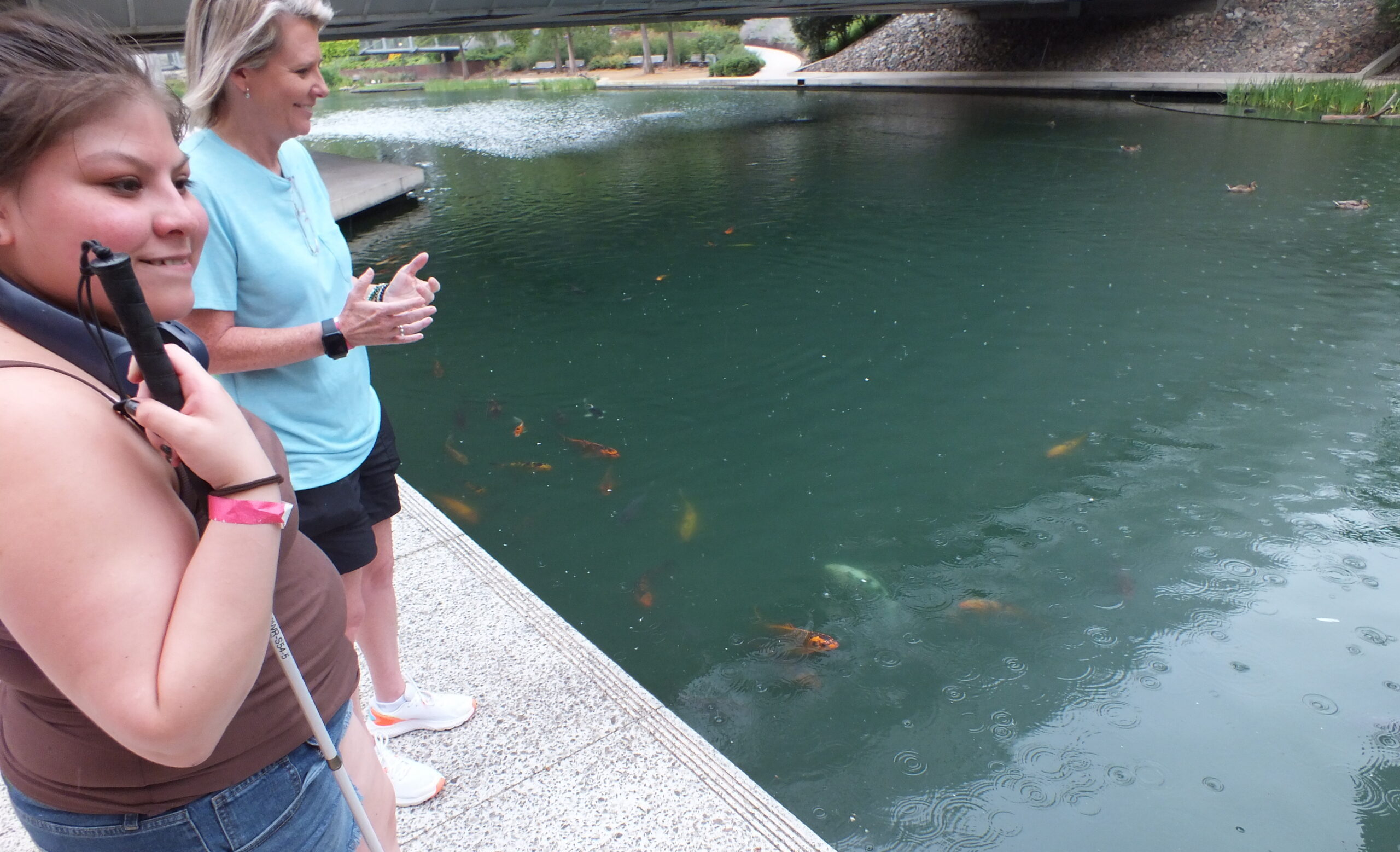 Serenity smiling at Myriad Gardens next to koi fish in pond and NewView's Christi Dixon.