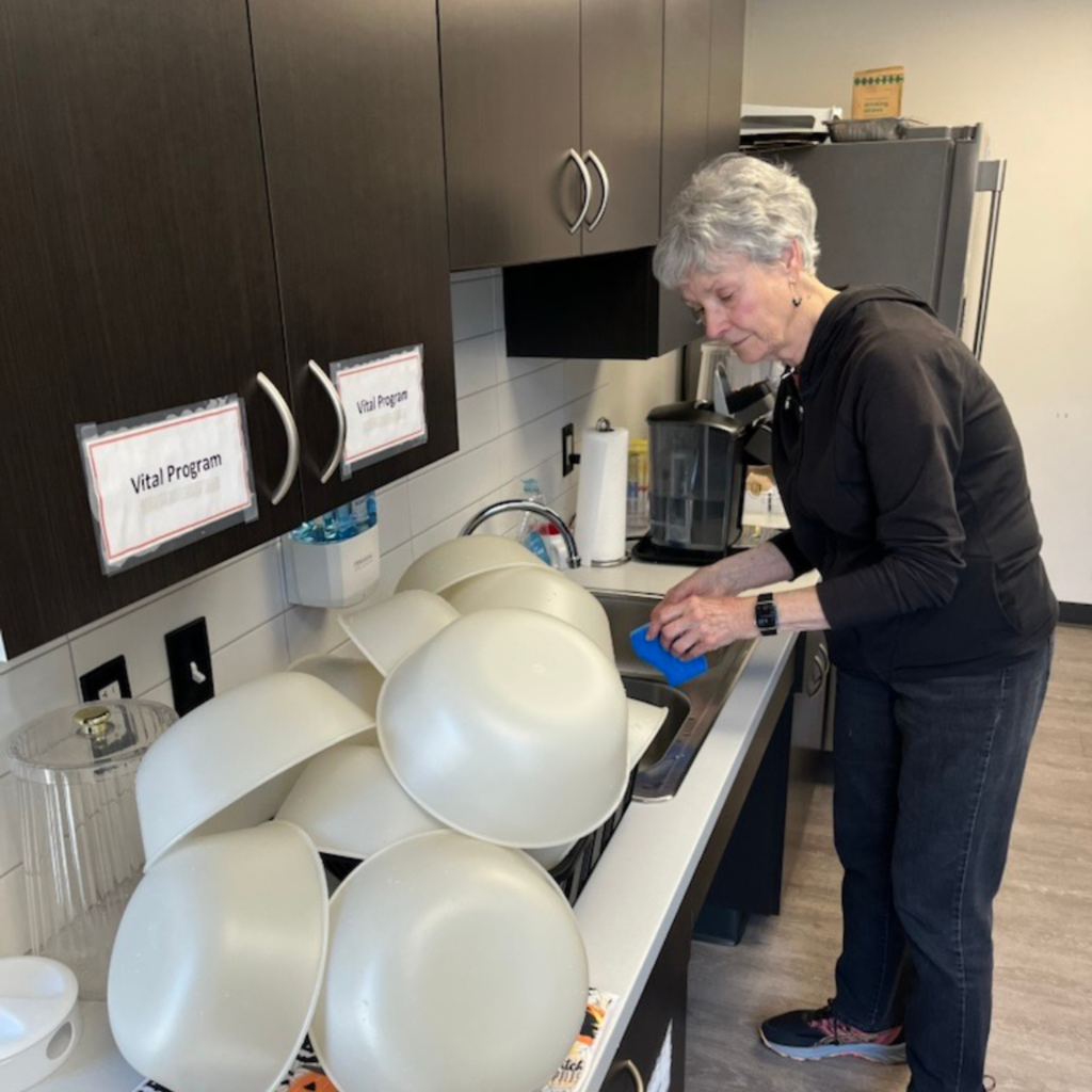 An older woman in the Classen Community Room kitchen calmly washing dishes.